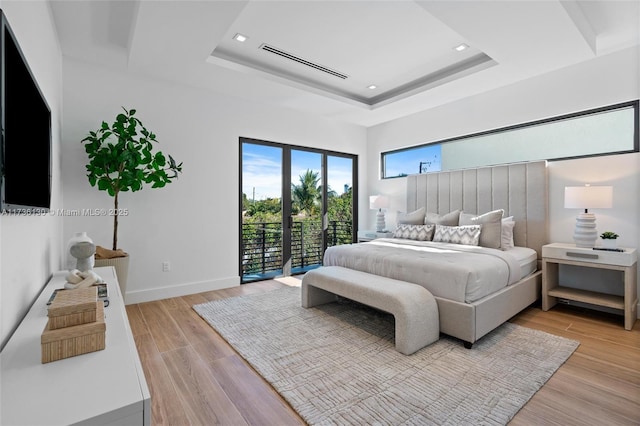 bedroom featuring access to outside, light wood-type flooring, and a tray ceiling