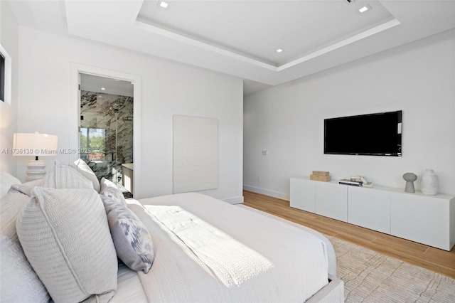 bedroom with ensuite bath, a raised ceiling, and hardwood / wood-style floors