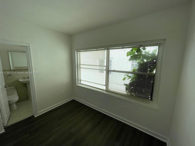 unfurnished bedroom featuring multiple windows, sink, dark wood-type flooring, and ensuite bathroom