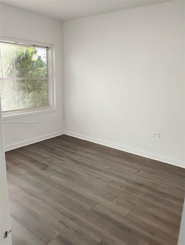 unfurnished room featuring baseboards and dark wood-type flooring