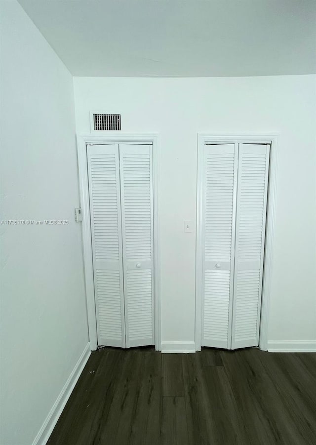 unfurnished bedroom featuring multiple closets and dark wood-type flooring