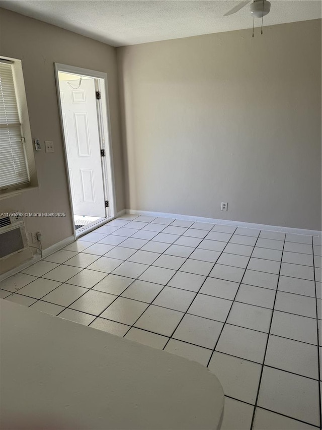 tiled spare room featuring ceiling fan, a wall mounted AC, and a textured ceiling