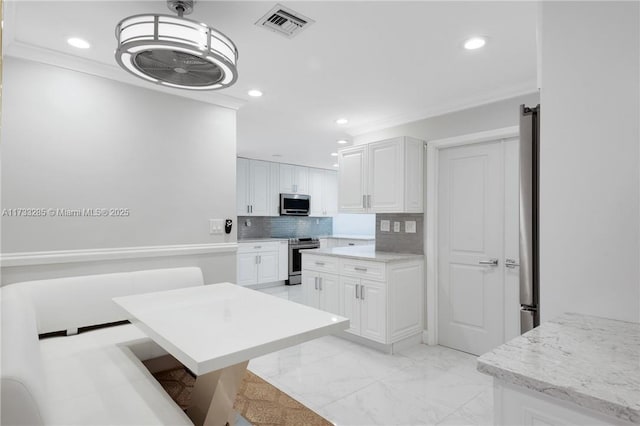 kitchen featuring backsplash, stainless steel appliances, ornamental molding, white cabinets, and decorative light fixtures