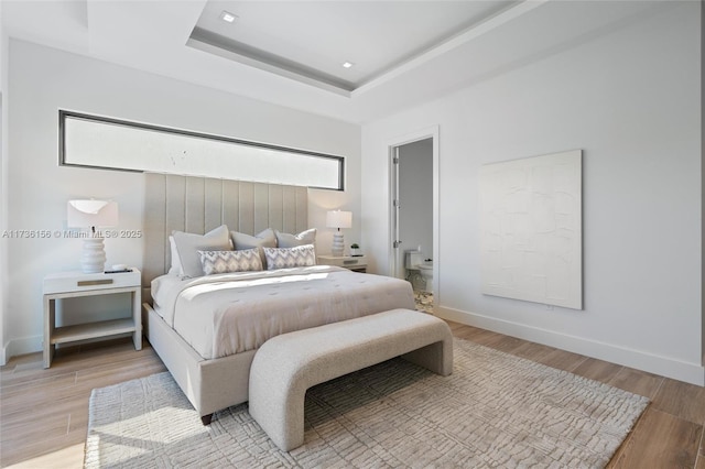 bedroom with a raised ceiling and light wood-type flooring