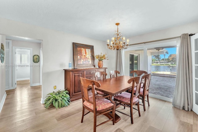 dining area featuring a water view, an inviting chandelier, and light hardwood / wood-style flooring