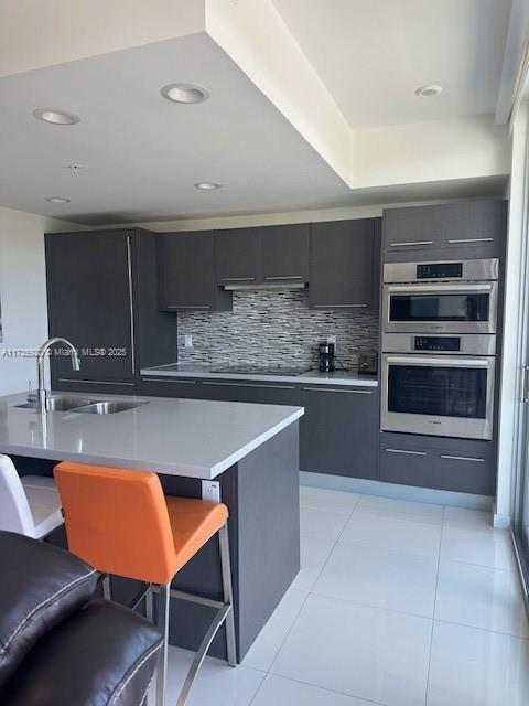 kitchen featuring a kitchen bar, sink, black electric cooktop, stainless steel double oven, and backsplash