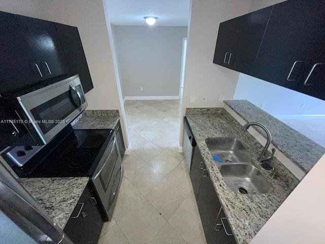 kitchen with a sink, stainless steel appliances, light stone countertops, and dark cabinetry