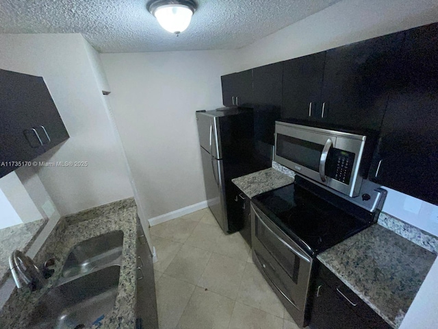 kitchen featuring a sink, a textured ceiling, appliances with stainless steel finishes, light stone countertops, and dark cabinets