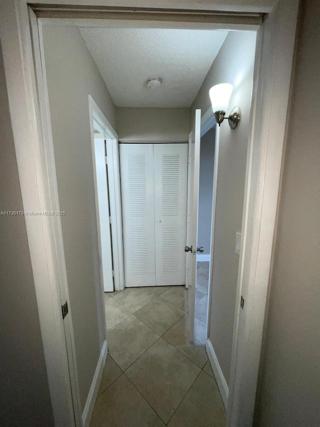 hall with light tile patterned flooring, baseboards, and a textured ceiling