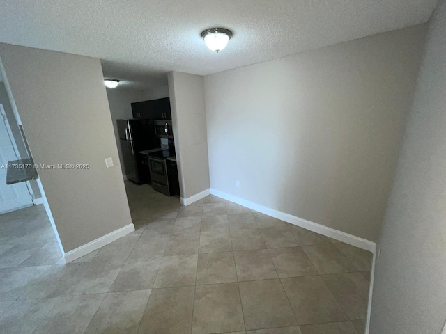 empty room featuring light tile patterned flooring, a textured ceiling, and baseboards