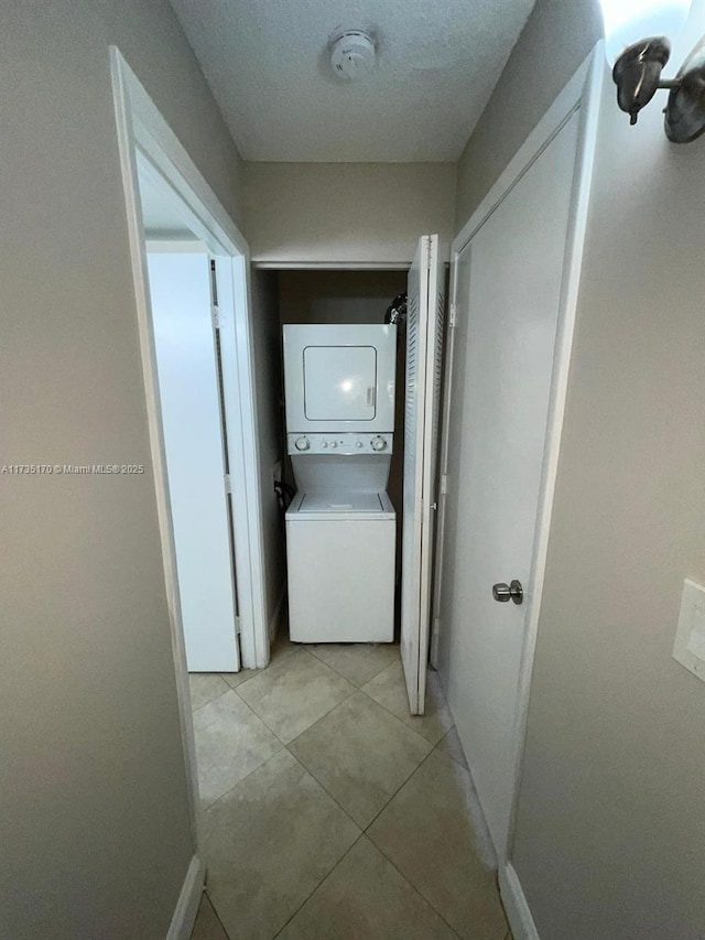 hallway with light tile patterned flooring, stacked washing maching and dryer, and baseboards