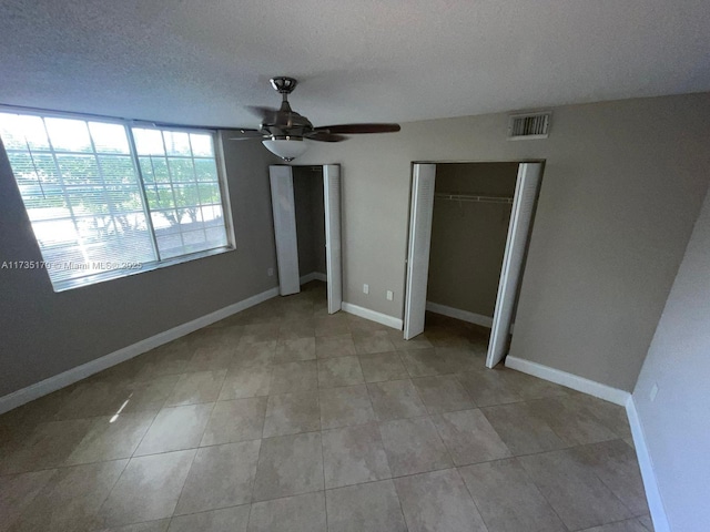 unfurnished bedroom featuring light tile patterned floors, a ceiling fan, baseboards, visible vents, and a textured ceiling