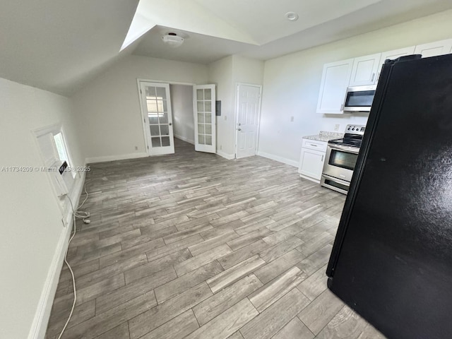 kitchen featuring lofted ceiling, white cabinetry, light wood-type flooring, appliances with stainless steel finishes, and light stone countertops