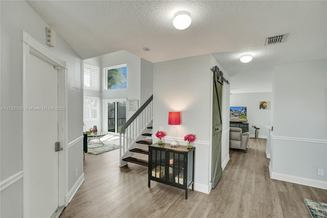 corridor featuring a barn door, light hardwood / wood-style flooring, and a textured ceiling