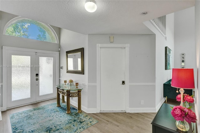 entryway with plenty of natural light, light hardwood / wood-style flooring, a textured ceiling, and french doors