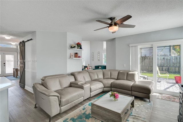 living room with ceiling fan, a barn door, a textured ceiling, and light wood-type flooring