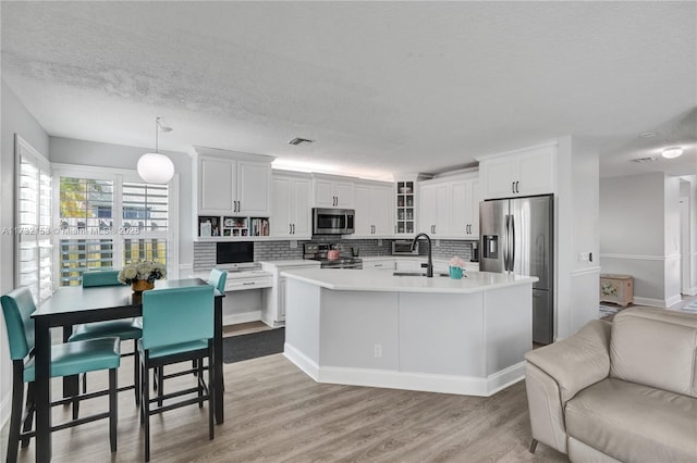 kitchen with sink, appliances with stainless steel finishes, white cabinetry, decorative light fixtures, and light wood-type flooring