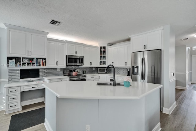 kitchen with white cabinetry, appliances with stainless steel finishes, a kitchen island with sink, and light hardwood / wood-style flooring