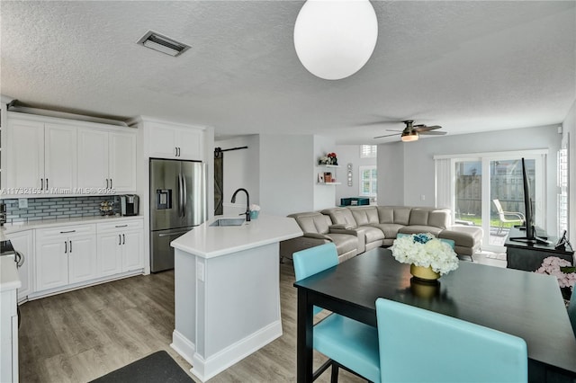 kitchen featuring sink, stainless steel fridge, white cabinets, a center island with sink, and a barn door