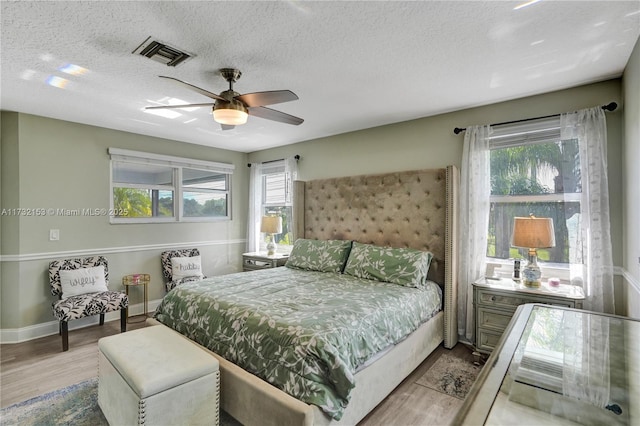 bedroom with ceiling fan, light hardwood / wood-style floors, and a textured ceiling