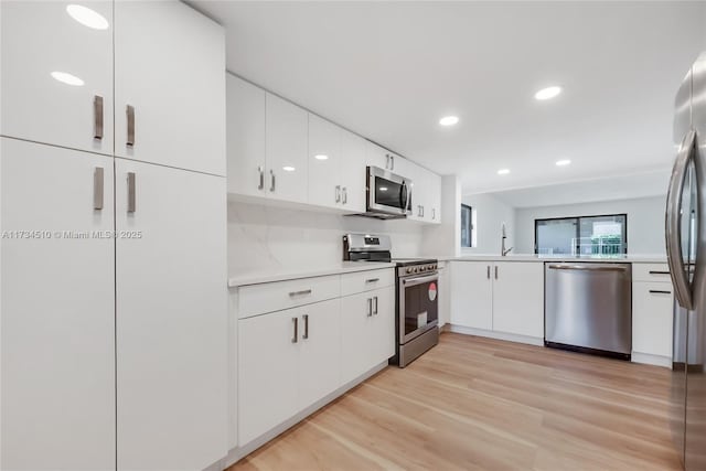 kitchen with sink, white cabinetry, light hardwood / wood-style flooring, appliances with stainless steel finishes, and kitchen peninsula