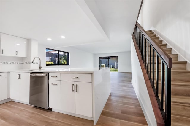 kitchen featuring sink, light wood-type flooring, stainless steel dishwasher, kitchen peninsula, and white cabinets