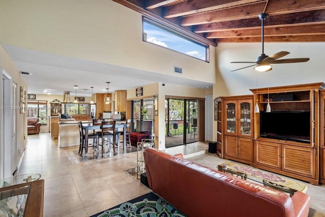 living room with a towering ceiling, ceiling fan, beam ceiling, and light tile patterned floors