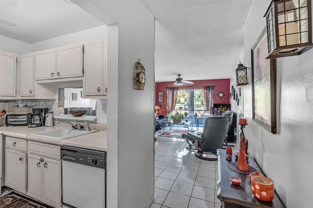 kitchen with white cabinetry, sink, dishwashing machine, light tile patterned floors, and a textured ceiling