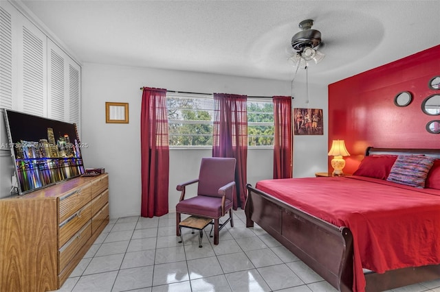 bedroom featuring ceiling fan, light tile patterned floors, and a textured ceiling