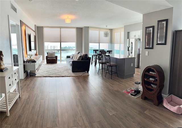 living room featuring dark wood-type flooring, a textured ceiling, and a wall of windows