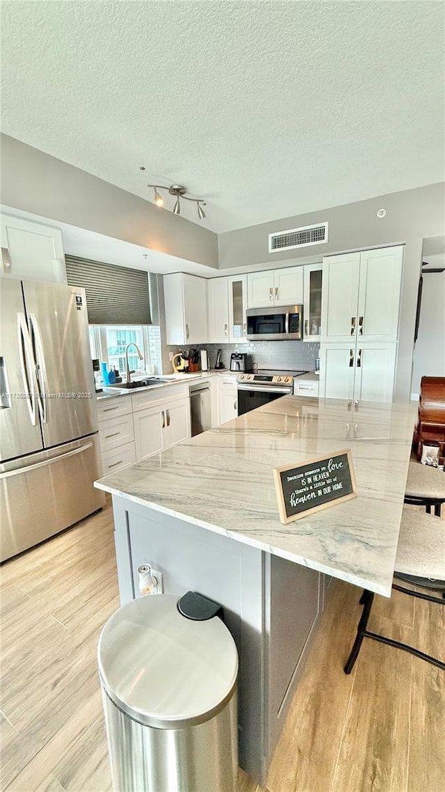 kitchen featuring light hardwood / wood-style flooring, white cabinetry, stainless steel appliances, light stone counters, and a textured ceiling