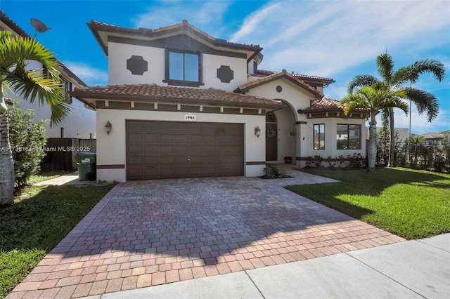 mediterranean / spanish home featuring a tile roof, fence, decorative driveway, a front yard, and stucco siding