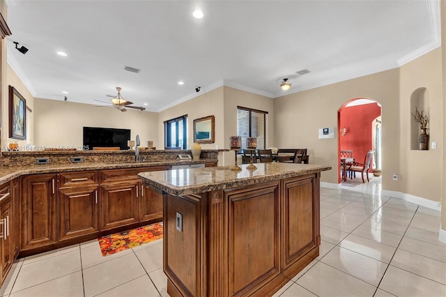 kitchen featuring light tile patterned floors, arched walkways, visible vents, ornamental molding, and a center island