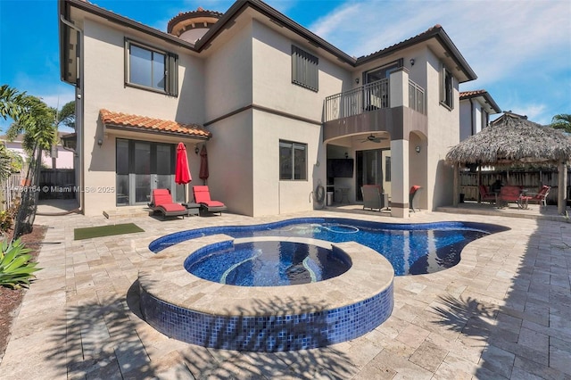 rear view of property featuring a swimming pool with hot tub, a gazebo, a patio area, and a balcony