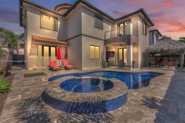 back of property at dusk featuring a patio, fence, a balcony, and stucco siding