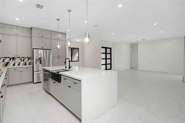 kitchen with gray cabinets, appliances with stainless steel finishes, pendant lighting, sink, and a center island with sink