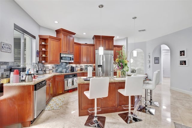 kitchen with a breakfast bar, decorative light fixtures, a center island, stainless steel appliances, and light stone countertops