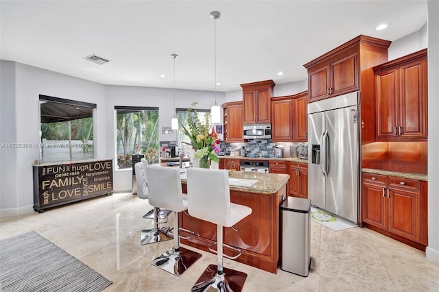 kitchen with a kitchen bar, light stone counters, hanging light fixtures, an island with sink, and stainless steel appliances