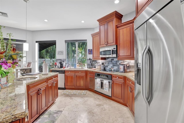 kitchen featuring hanging light fixtures, light stone countertops, appliances with stainless steel finishes, and sink