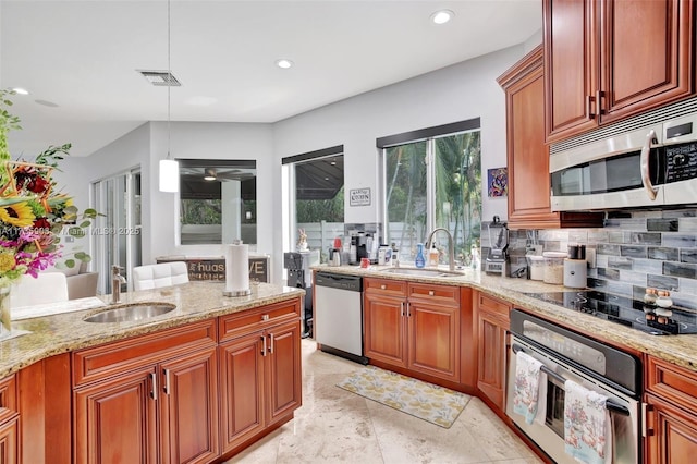 kitchen featuring stainless steel appliances, sink, light stone counters, and decorative light fixtures