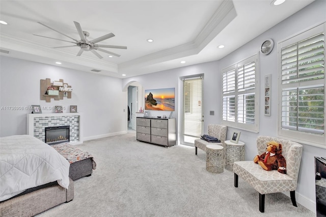 bedroom with light carpet, a tray ceiling, ornamental molding, and a tile fireplace