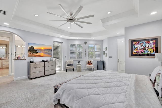 carpeted bedroom featuring crown molding, ensuite bath, a tray ceiling, and ceiling fan