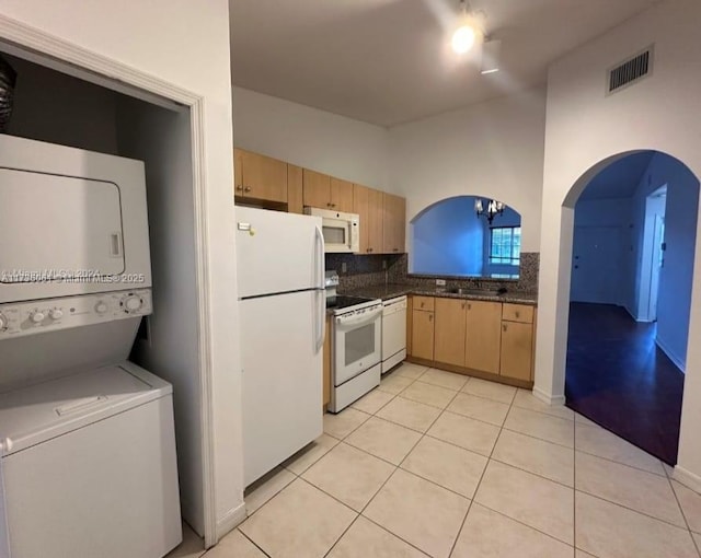 kitchen with light tile patterned flooring, sink, tasteful backsplash, white appliances, and stacked washer / dryer