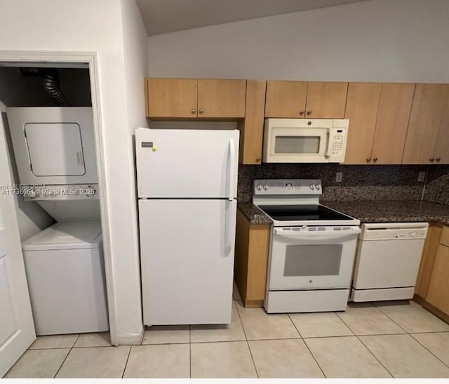 kitchen featuring white appliances, stacked washer / dryer, vaulted ceiling, and dark stone countertops