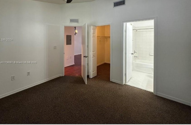 unfurnished bedroom featuring electric panel, ensuite bathroom, dark colored carpet, a walk in closet, and a closet