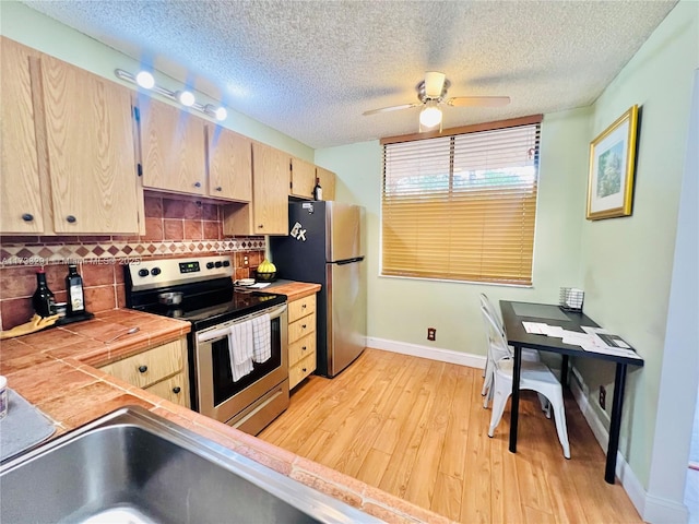 kitchen featuring light brown cabinetry, tasteful backsplash, light hardwood / wood-style flooring, a textured ceiling, and appliances with stainless steel finishes