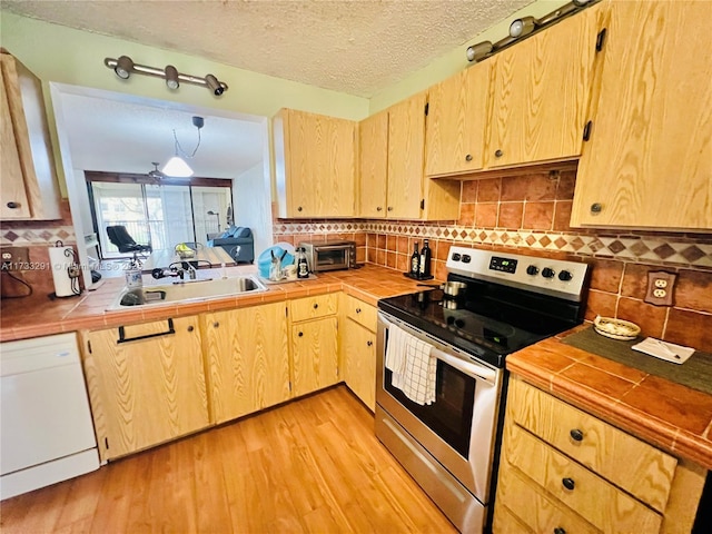 kitchen with stainless steel electric range, dishwasher, sink, tile counters, and light hardwood / wood-style flooring