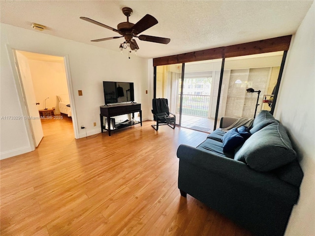 living room with ceiling fan, a textured ceiling, and light wood-type flooring