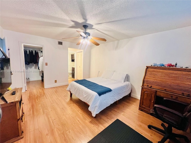 bedroom with connected bathroom, light wood-type flooring, a walk in closet, ceiling fan, and a textured ceiling