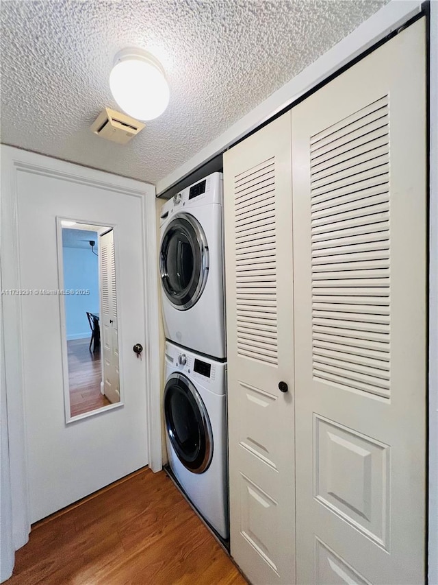 clothes washing area with stacked washer and dryer, hardwood / wood-style flooring, and a textured ceiling